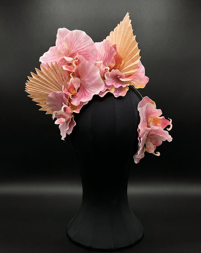 A decorative floral orchid fascinator with ecru fan-like leaves with orchid side comb, displayed on a black mannequin head against a dark studio background.