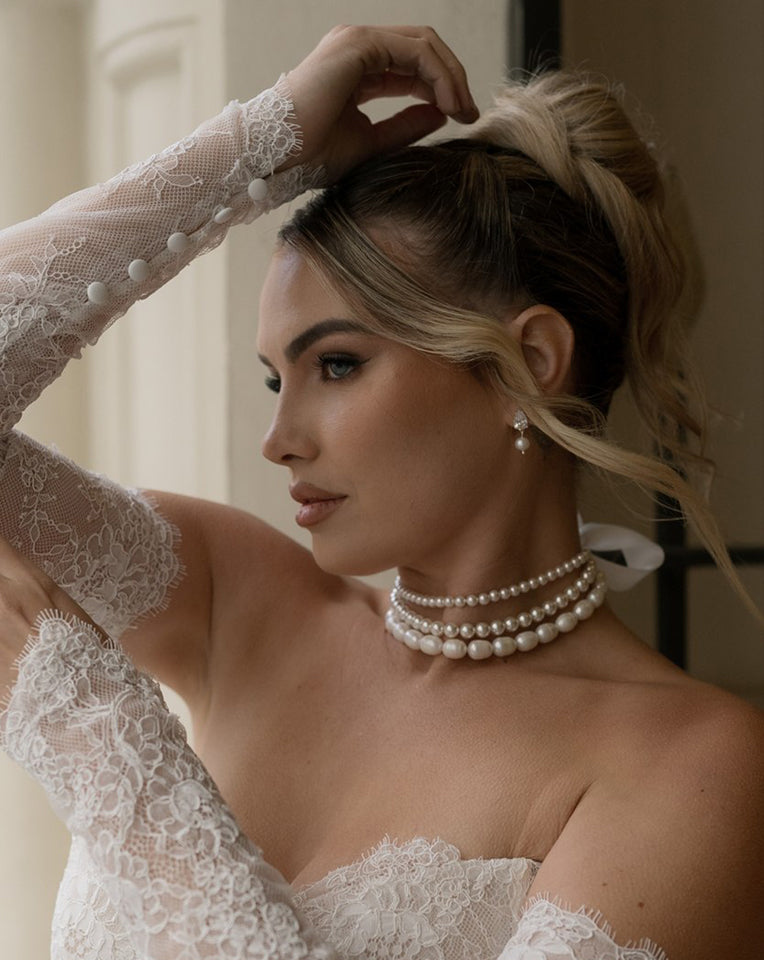 blonde bride with updo wearing a three row pearl choker and dainty sutton earrings with lace bridal sleeves - kezani jewellery