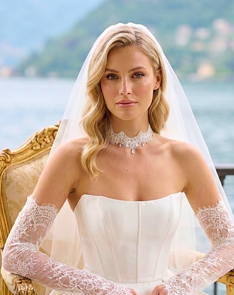 Beautiful bride in corset bodice with lace sleeves wearing a delicate lace choker by Kezani jewellery sitting in chair at lake como