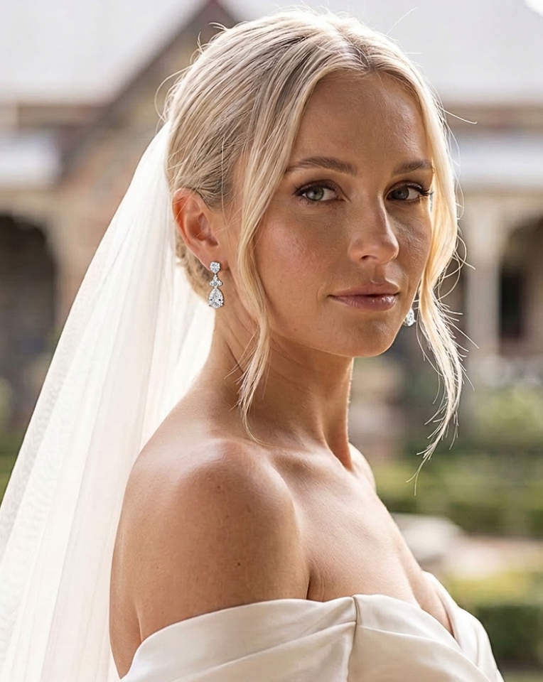Blonde bride wearing crystal pear drop earrings with satin off-shoulder bridal gown