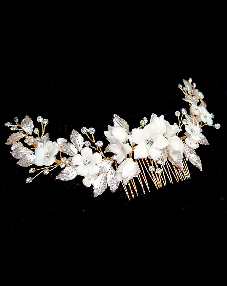 A bridal headpiece featuring a floral design with porcelain flowers and rose gold metallic leaf accents, designed to be worn with a hairstyle.