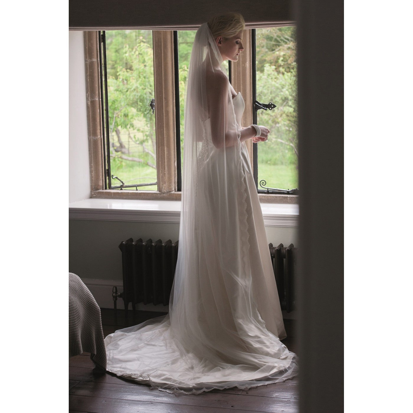 A bride full length veil scallop lace edge veil called "Beauty" from Kezani jewellery that gathers to a circle around her on the floor.