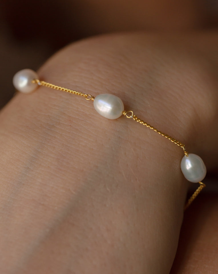 close up of gold faith bracelet on wrist with chain alternating with dainty freshwater pearls 