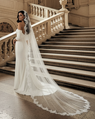 bride standing at bottom of staircase wearing an off shoulder satin wedding gown with a long cathedral length lace edge mantilla