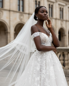 Woman in a white wedding dress with a long two tier veil with crinoline edging standing in front of an architectural building.