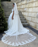 full back view of a bride standing on stairs with a beautiful two tier katia full wedding veil that has a deep chantilly lace style trim around the border. Showing 3m veil with train of wedding gown