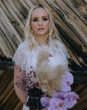 image of bride model in front of barn door holding flower bouquet and wearing bridal earings white opal boho earing called pipa by kezani jewellery